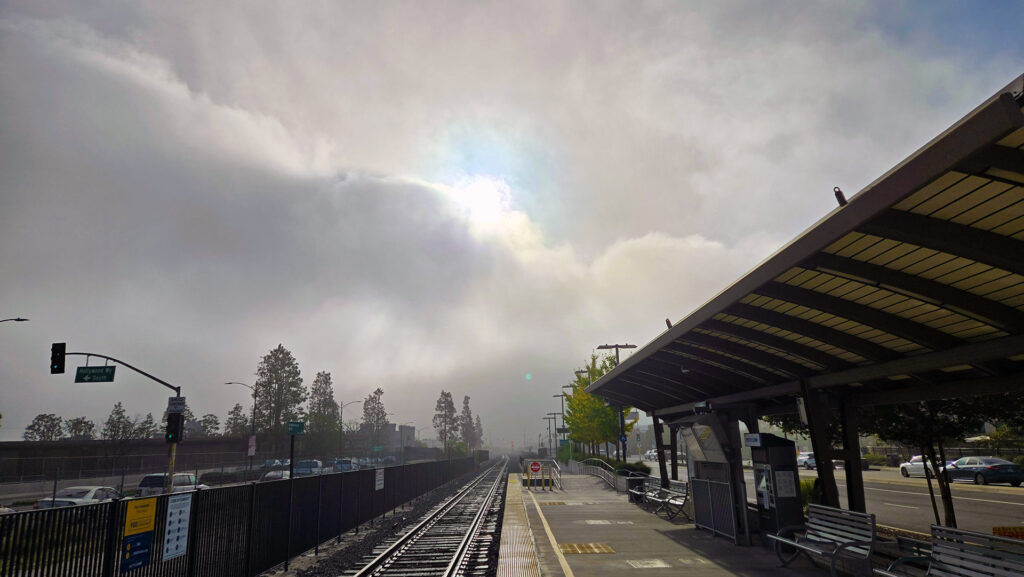 Standing on a train platform with a fog bank breaking with the sun popping out.