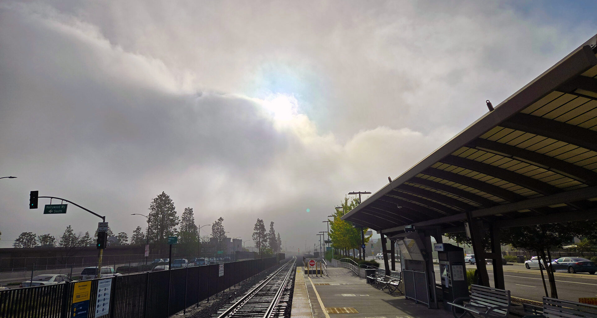 Standing on a train platform with a fog bank breaking with the sun popping out.